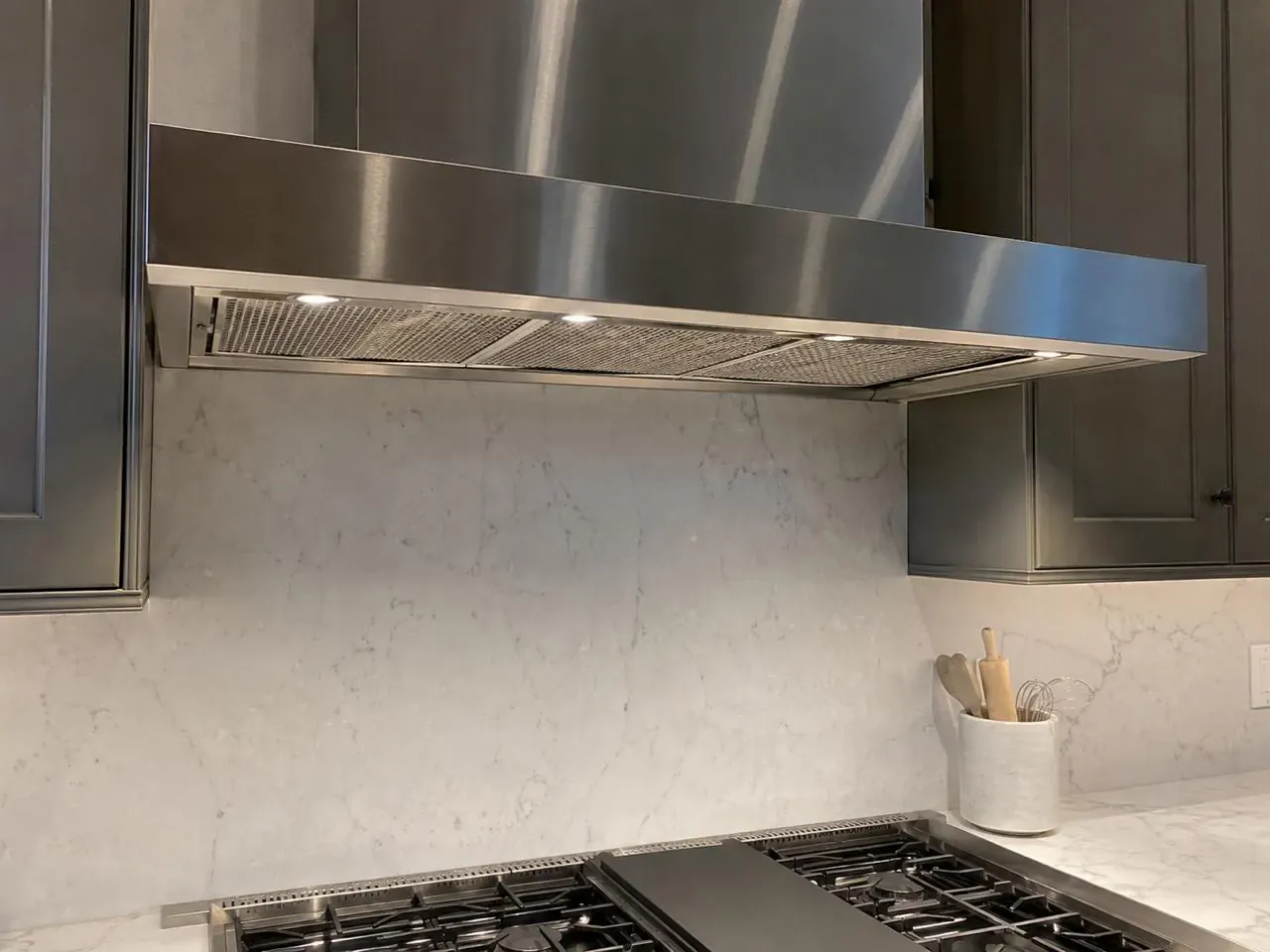 Stainless range hood over a professional gas cooktop with a marble backsplash