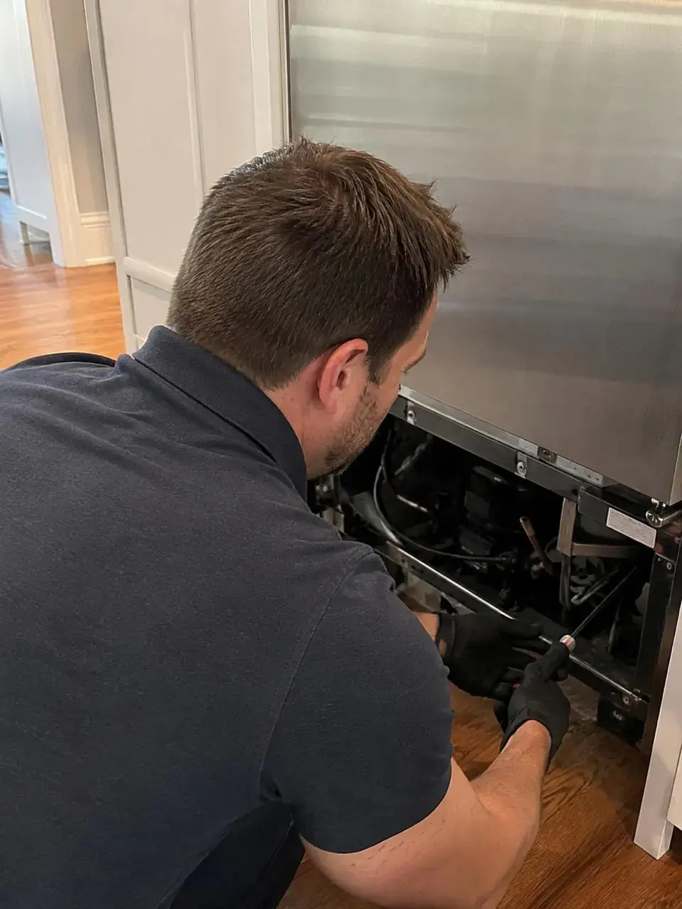 Technician servicing the sealed system at the back of a built-in refrigerator
